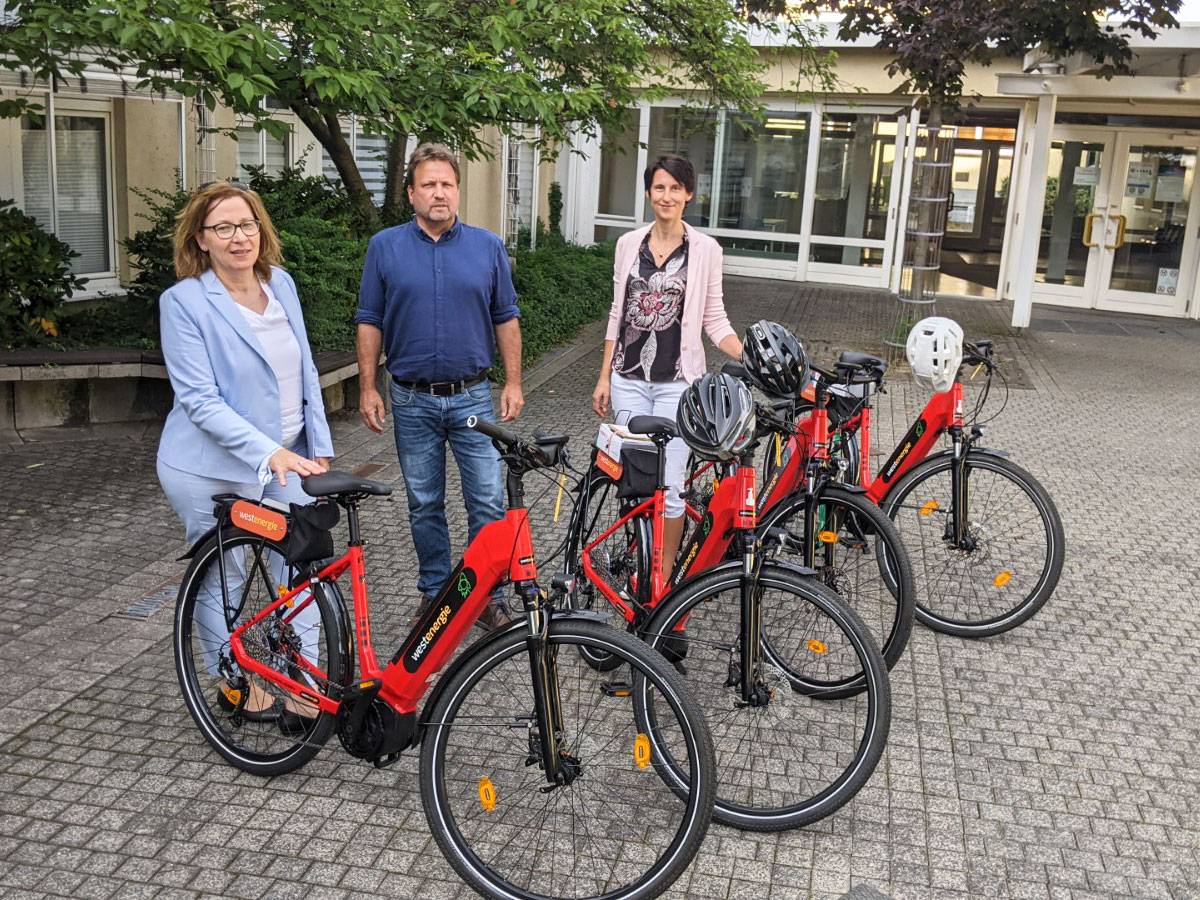 Elisabeth Schlüter, Westenergie Kommunalmanagerin, Bürgermeister Lutz Wagner sowie Klimaschutzmanagerin Antje Fehr mit den vier neuen E-Bikes vor dem Eingangsbereich am Verwaltungsgebäude Thomasberg.