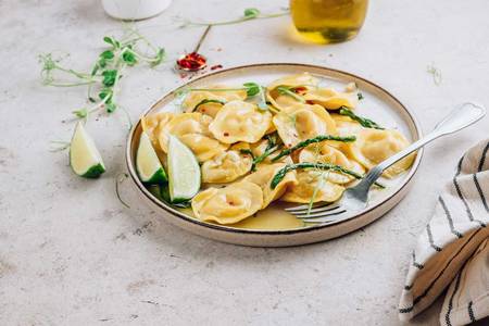 Ein Teller mit Ravioli, grünem Spargel auf einem Tisch mit Zitrone und Geschirrtuch