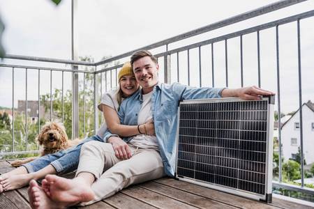 Ein junges Paar sitzt auf dem Balkon neben einem Steckersolargerät