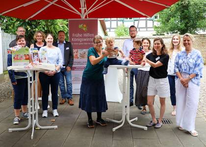 Gruppenbild aller Beteiligten. Die beiden Babies sitzen fröhlich auf dem Tisch