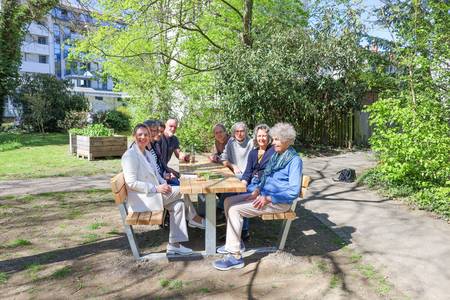 Eine Gruppe sitzt auf einer Holz-Sitzgruppe in einem Park