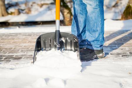 Ein Ausschnitt einer Schneeschaufel, mit der Schnee auf einem Gehweg geräumt wird