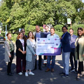 Die Stadt Königswinter freut sich zusammen mit Vertreterinnen und Vertretern von go.Rheinland, der Bezirksregierung Köln und der Baufirma Wurzel über die Förderungen und den Start der Maßnahmen an der Rheinuferstraße. © Stadt Königswinter Gruppenbild am Rheinufer vor der Haltestelle in Niederdollendorf