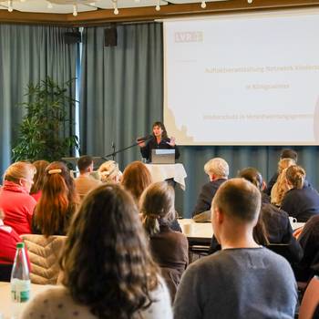 Über 100 Fachkräfte aus Medizin, Bildung, Jugendhilfe, Beratung, Staatsanwaltschaft und Polizei kamen beim Auftakt „Netzwerk Kinderschutz“ zusammen, um die Weichen für eine engere Zusammenarbeit zu stellen. © Stadt Königswinter/Pressestelle In einem Saal referiert eine Frau, vor ihr eine Gruppe von Menschen