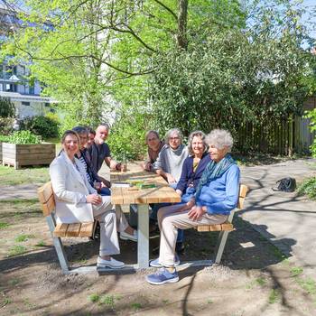 Eine Gruppe sitzt auf einer Holz-Sitzgruppe in einem Park