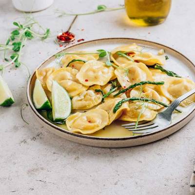 Ein Teller mit Ravioli, grünem Spargel auf einem Tisch mit Zitrone und Geschirrtuch