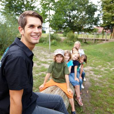 Junger Mann sitzt lachend vor einer Gruppe von Kindern