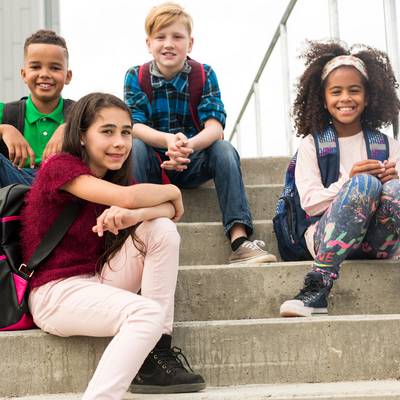 Vier Kinder sitzen auf einer Schultreppe und schauen nach vorne