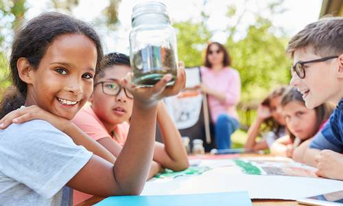 Eine Gruppe Kinder erarbeitet ein Projekt an einem Tisch in der Natur