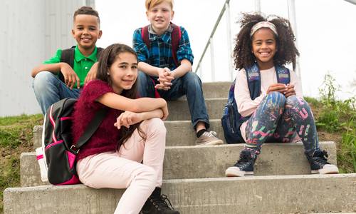 Vier Kinder sitzen auf einer Schultreppe und schauen nach vorne