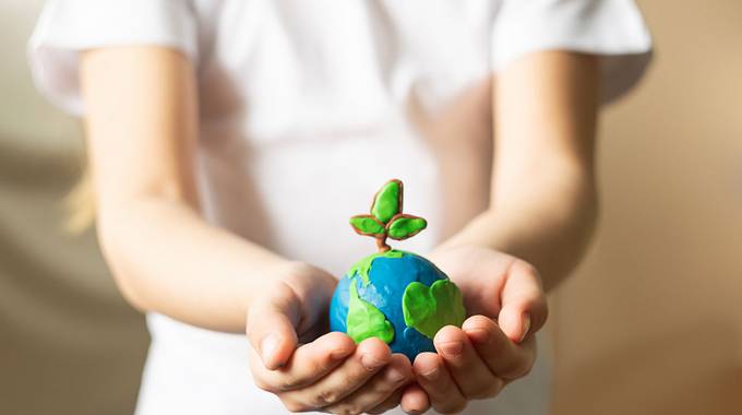 Eine Kinderhand hält eine Weltkugel aus Knete in der Hand, aus der eine Pflanze wächst