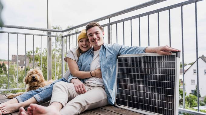 Ein junges Paar sitzt auf dem Balkon neben einem Steckersolargerät