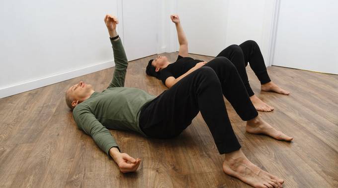 Zwei Personen liegen auf dem Holzboden und machen Gymnastik