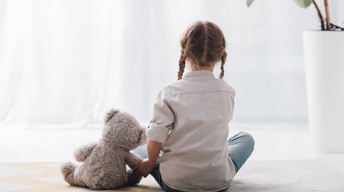 Mädchen mit Teddy © LIGHTFIELD-STUDIOS - stock.adobe.com Ein Mädchen sitzt mit seinem Teddy und dem Rücken zum Betrachter auf dem Boden
