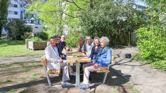 Eine Gruppe sitzt auf einer Holz-Sitzgruppe in einem Park