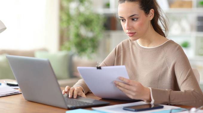 Junge Frau sitzt vor dem Laptop mit einem Formular in der Hand