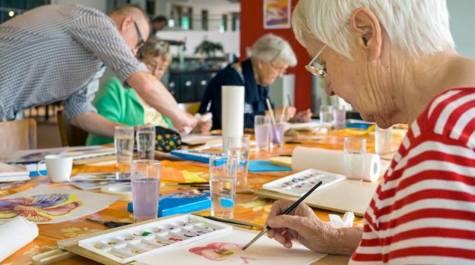 Seniorin malt am Tisch ein Aquarell einer Blume