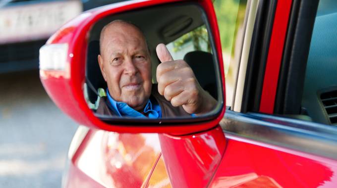 Senior schaut durch den Rückspiegel aus dem Auto und zeigt Daumen hoch