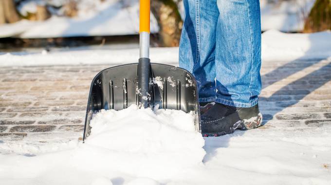 Ein Ausschnitt einer Schneeschaufel, mit der Schnee auf einem Gehweg geräumt wird