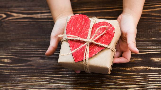 Eine Kinderhand hält ein Paket mit einem roten Herzen